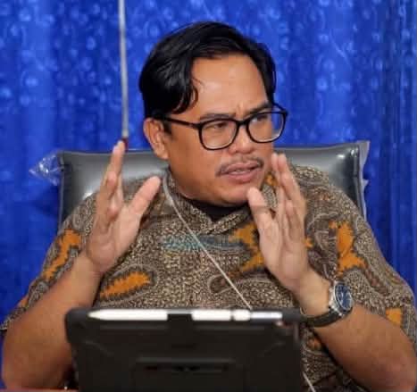 Man in glasses gesturing while speaking at a desk